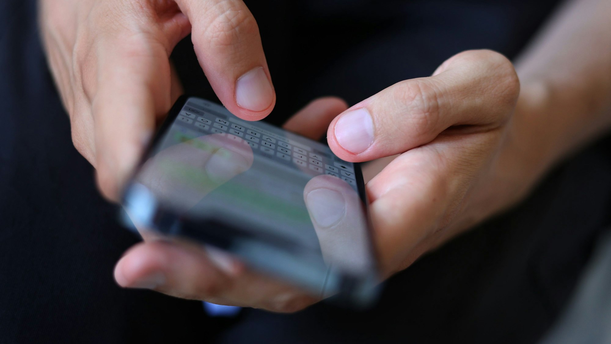 Ein junger Mann tippt auf einem Smartphone eine WhatsApp Nachricht.