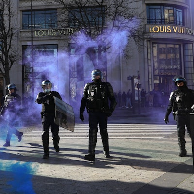 Frankreich, Paris: Polizisten gehen auf der Avenue des Champs-Elysees durch sich ausbreitendes Tränengas.