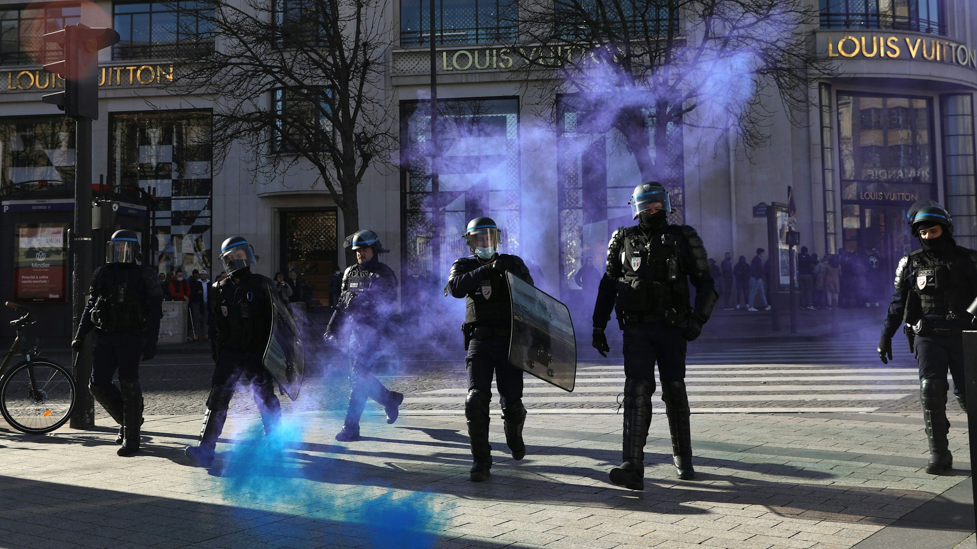 Frankreich, Paris: Polizisten gehen auf der Avenue des Champs-Elysees durch sich ausbreitendes Tränengas.