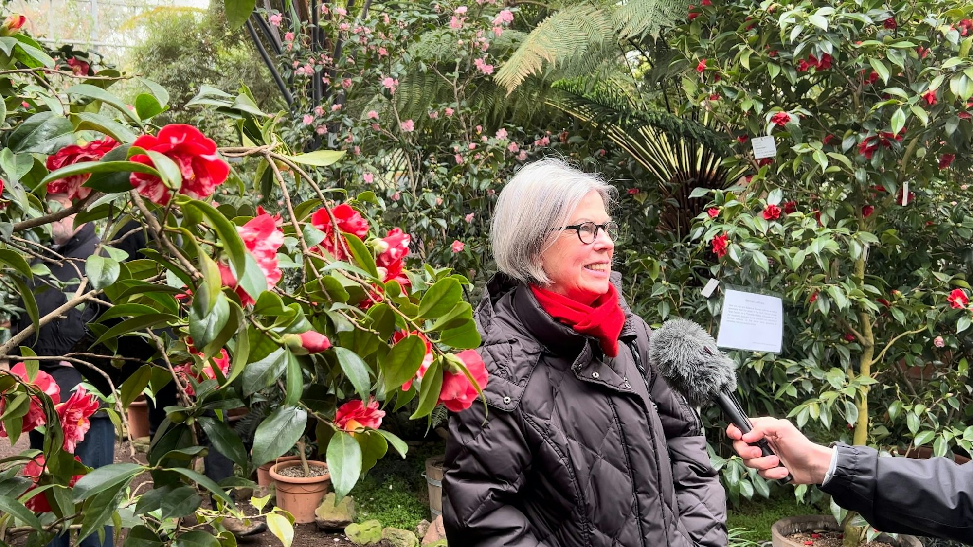 Eine Frau in schwarzer Jacke steht vor einem Blumenstrauch.