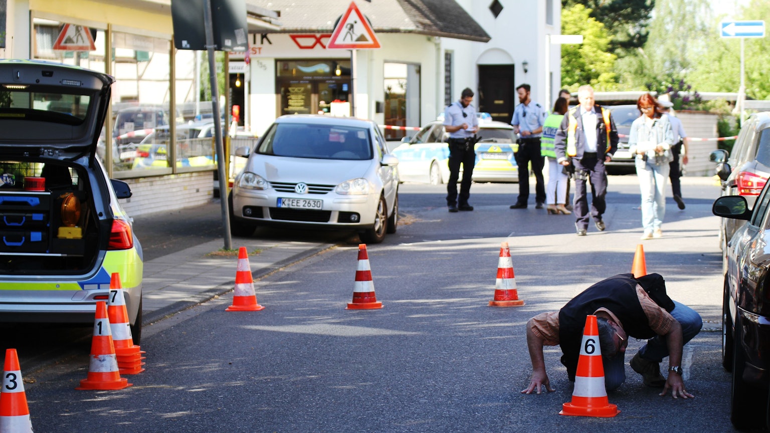 Nach einer Schießerei in Porz-Wahn auf dem Fasanenweg im Mai 2016 sucht ein Polizist unter einem Auto nach Projektilen.
