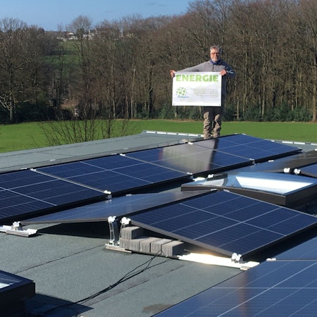 Stefan Häusler, Vorsitzender der Klimafreunde Rhein-Berg, steht auf einer Fotovoltaikanlage und hält ein Schild mit der Aufschrift „Energie“.