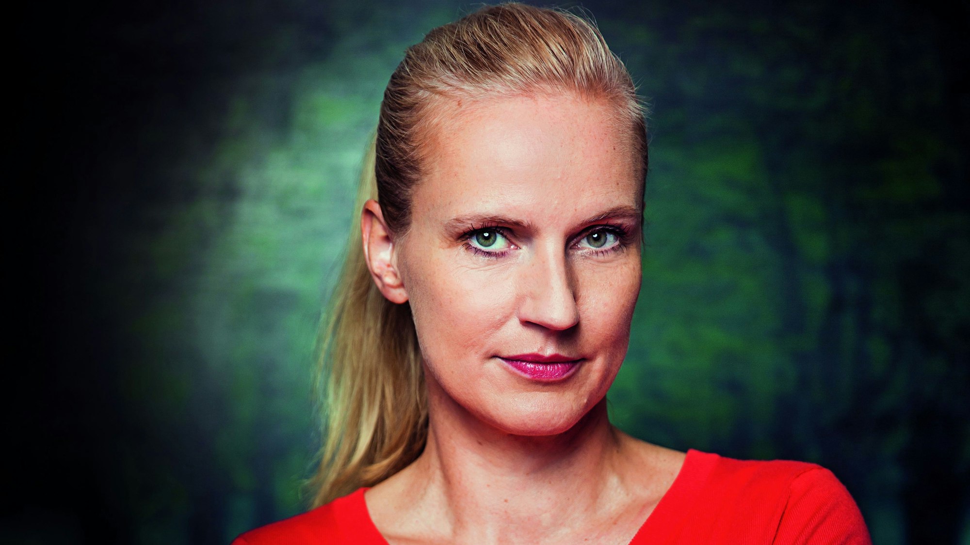 Autorin Christine Drews trägt einen roten Pullover und blickt in die Kamera.