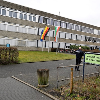 13.03.2023, Nordrhein-Westfalen, Freudenberg: Mitarbeiter des Ordnungsamtes stehen vor dem Schulzentrum des ermordeten Mädchens. Die Schule hat geöffnet, die Fahnen sind auf Halbmast geflaggt.