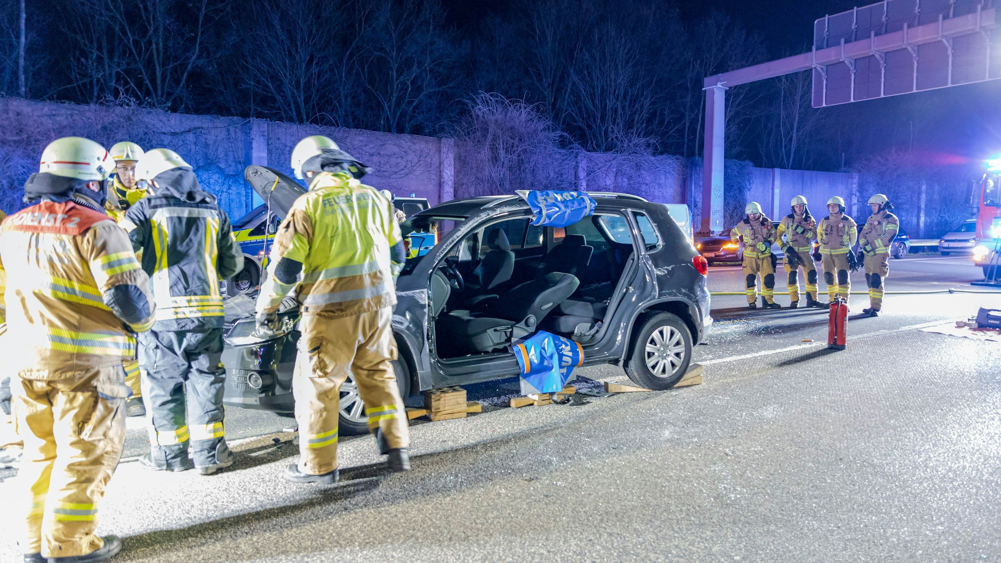 Feuerwehrleute stehen an einem aufgeschnittenen Auto auf der Autobahn. im Hintergrund stehen ein Feuerwehrfahrzeug und ein Polizeiwagen.