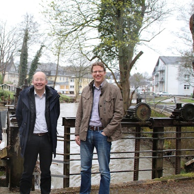 Die drei Männer sind vor einem Stauwehr zu sehen, dahinter das rauschende Wasser der Urft.