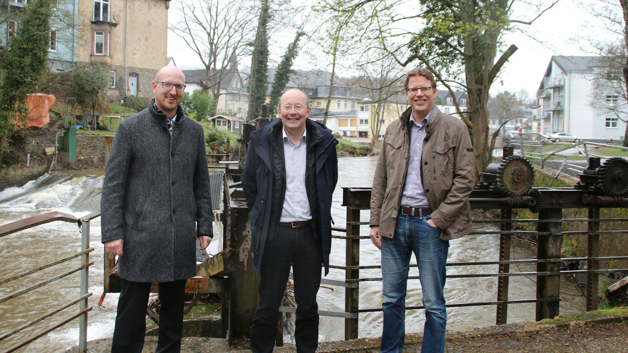 Die drei Männer sind vor einem Stauwehr zu sehen, dahinter das rauschende Wasser der Urft.