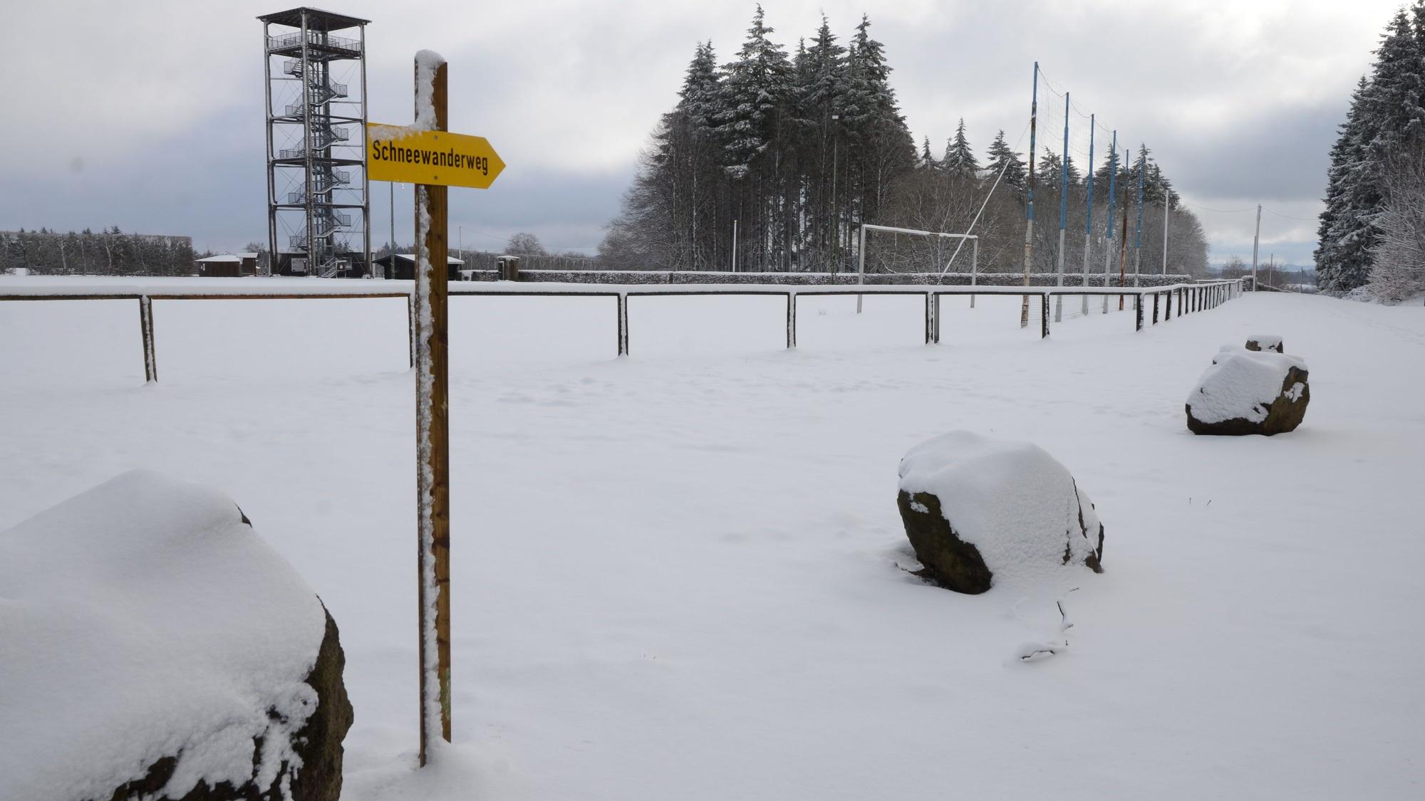 Ein schneebedeckter Weg. Ein Schild weist auf einen Schneewanderweg hin.