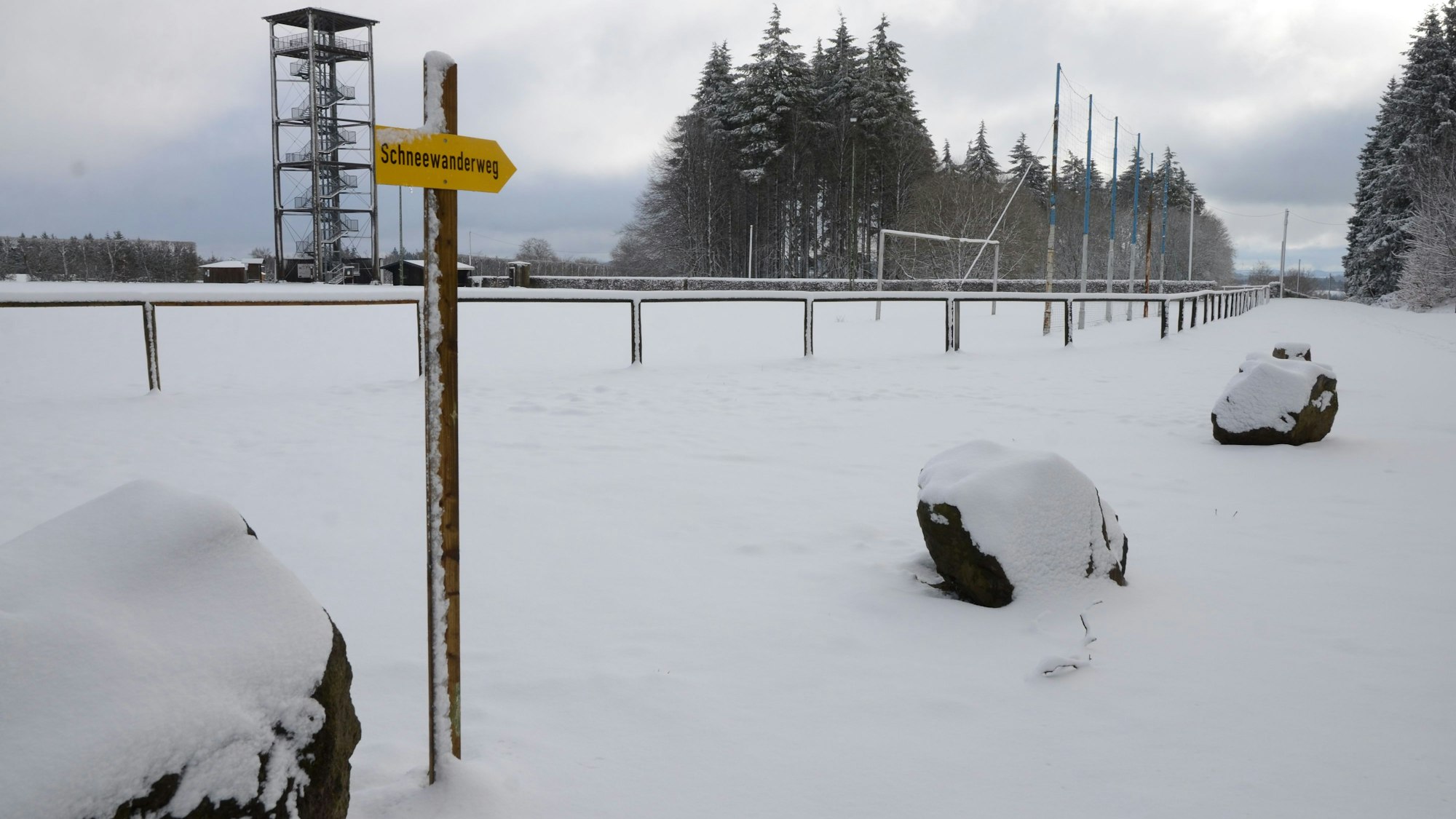 Ein schneebedeckter Weg. Ein Schild weist auf einen Schneewanderweg hin.