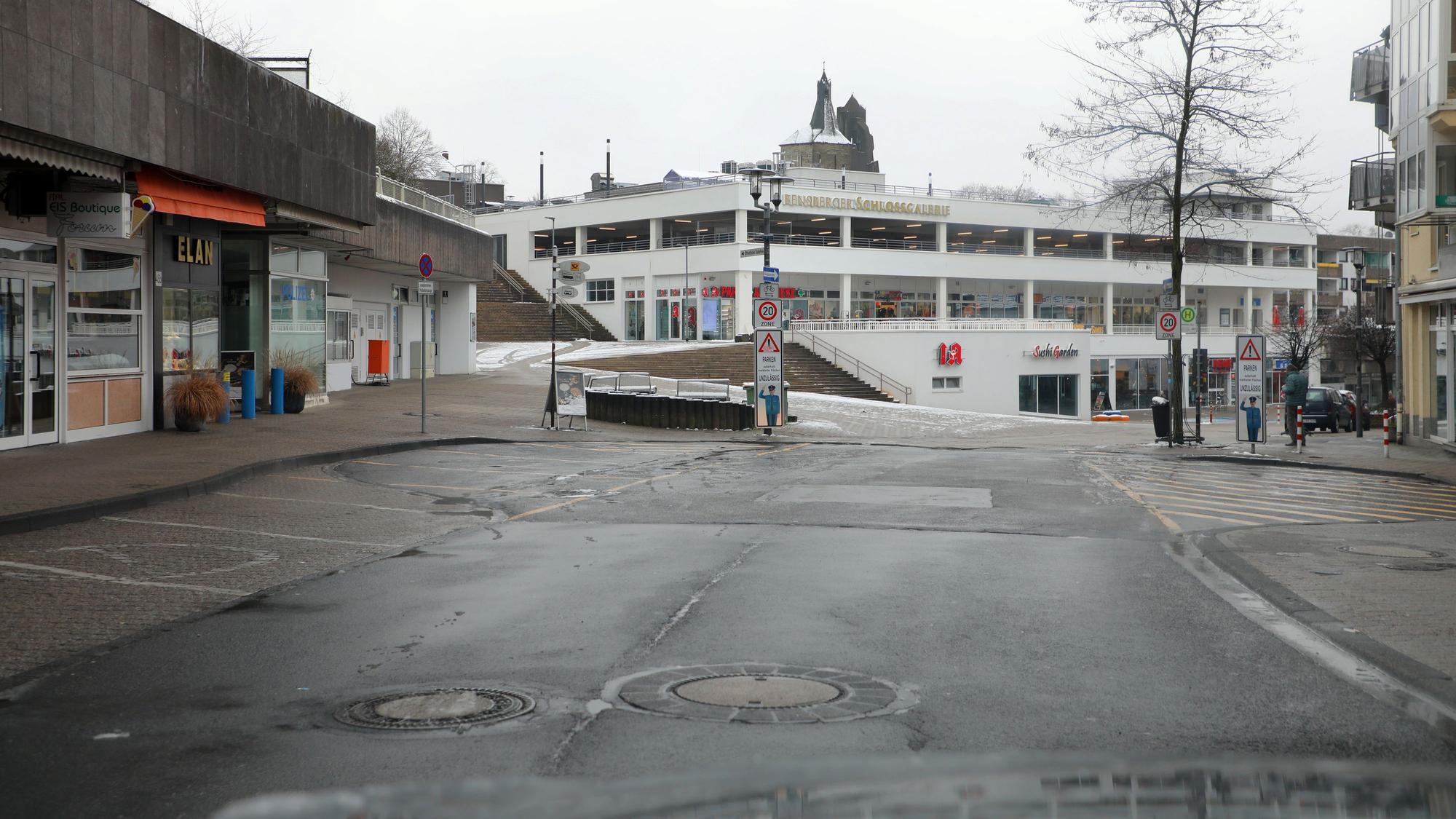 Durch die Frontscheibe eines Autos ist die Schloßstraße und an ihr das Einkaufszentrum Schlossgalerie zu sehen. Zahlreiche Parktaschen neben der Fahrbahn sind frei.