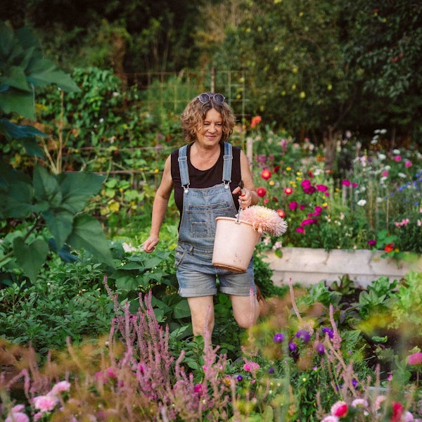 Anja Klein trägt eine Jeans-Latzhose und ein schwarzes T-Shirt und hält einen rosafarbenen Eimer mit Blumen in der Hand.