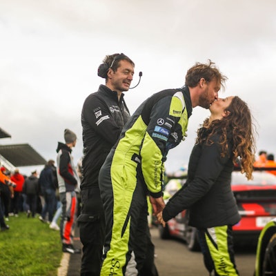 Die Rennfahrer Schreiner und Terting küssen sich neben den Autos.