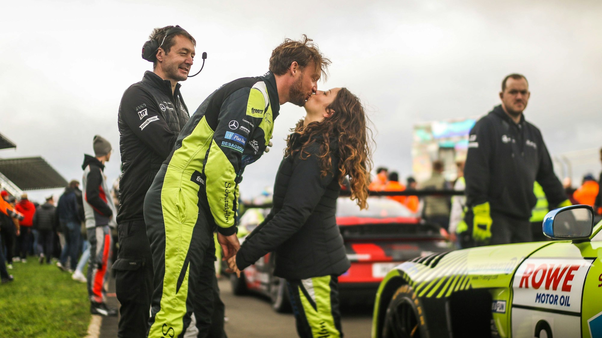 Die Rennfahrer Schreiner und Terting küssen sich neben den Autos.