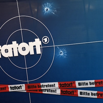 Auf einer Fotorückwand sind das Logo der ARD-Fernsehreihe „Tatort“, Einschusslöcher und Absperrband abgebildet.