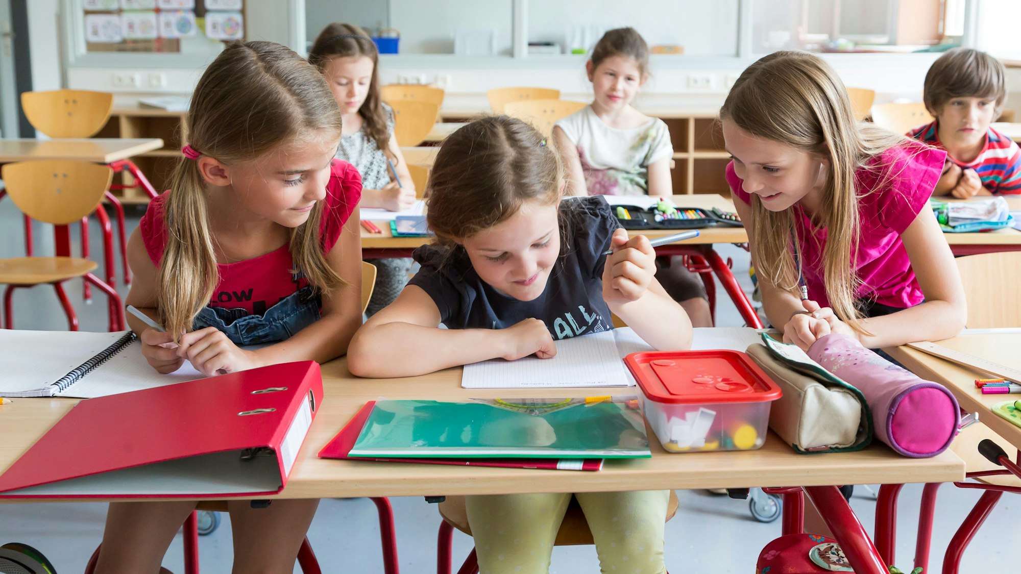Drei Mädchen in der Grundschule machen zusammen Aufgaben in der Klasse.