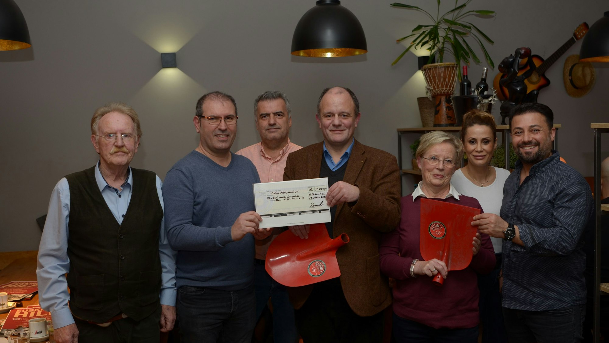 Mitglieder des Lions-Club in Euskirchen-Veybach halten einen Spendencheck und rote Schaufeln ins Bild.