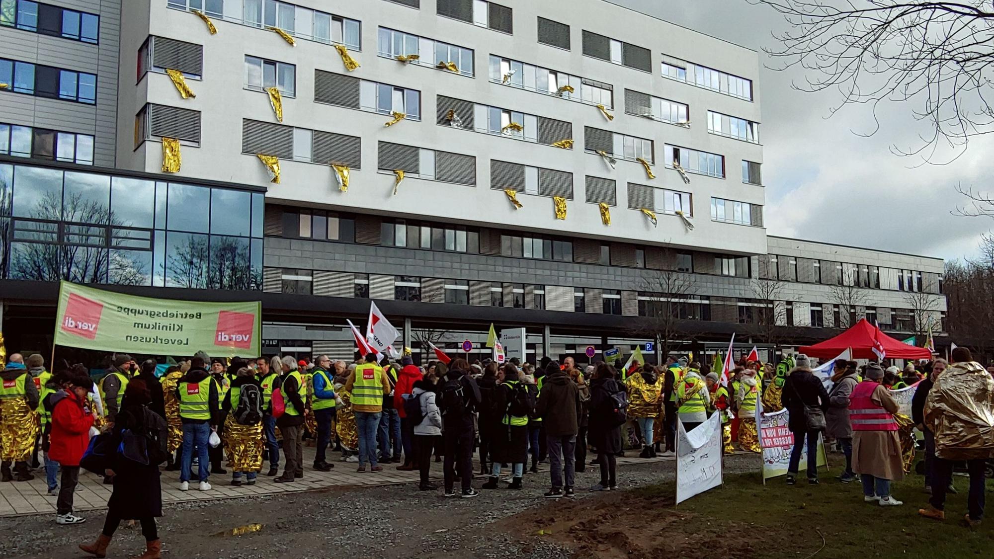 Menschen in Warnwesten und mit Protestschildern vor einem Krankenhausgebäude