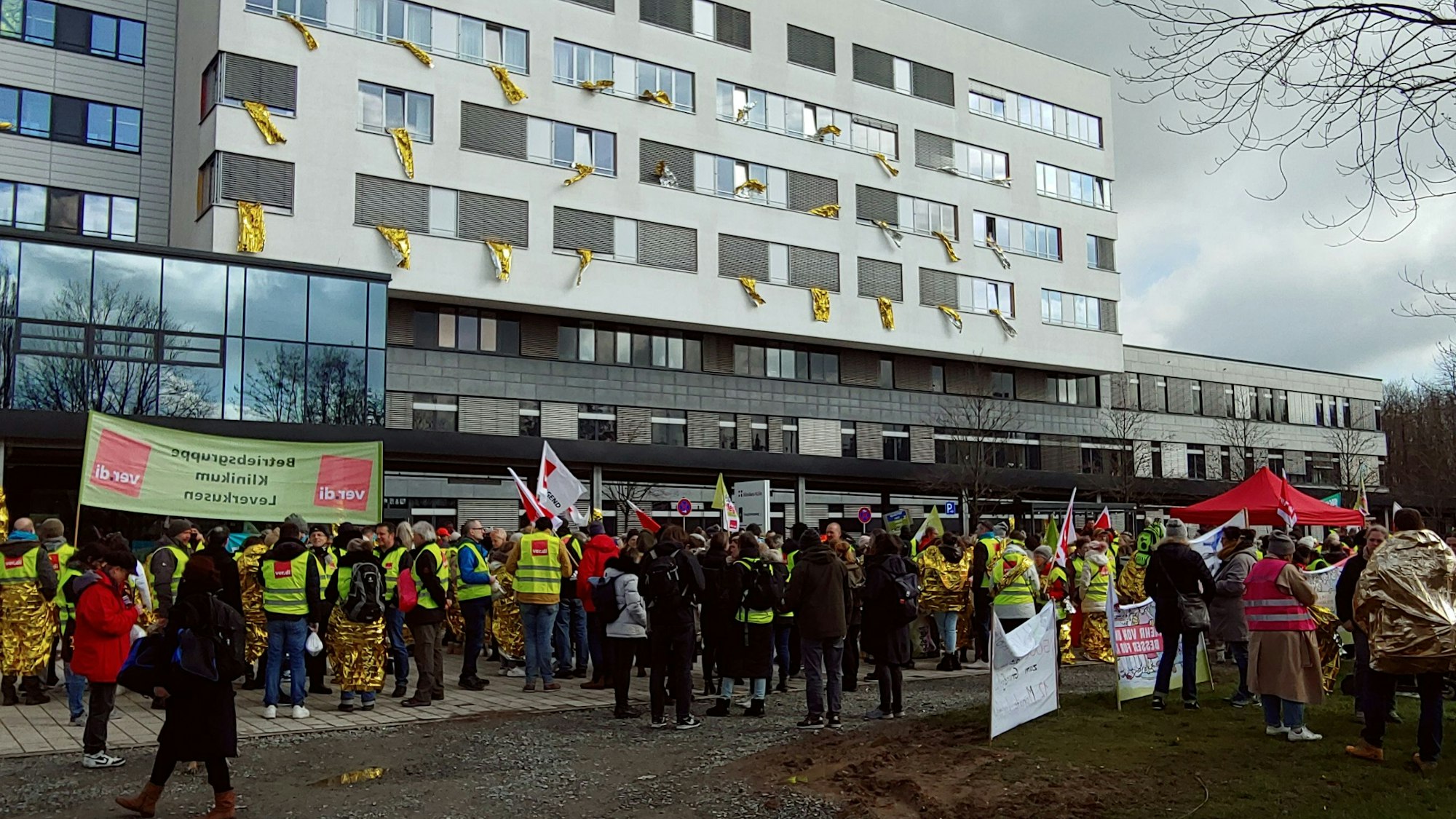 Menschen in Warnwesten und mit Protestschildern vor einem Krankenhausgebäude