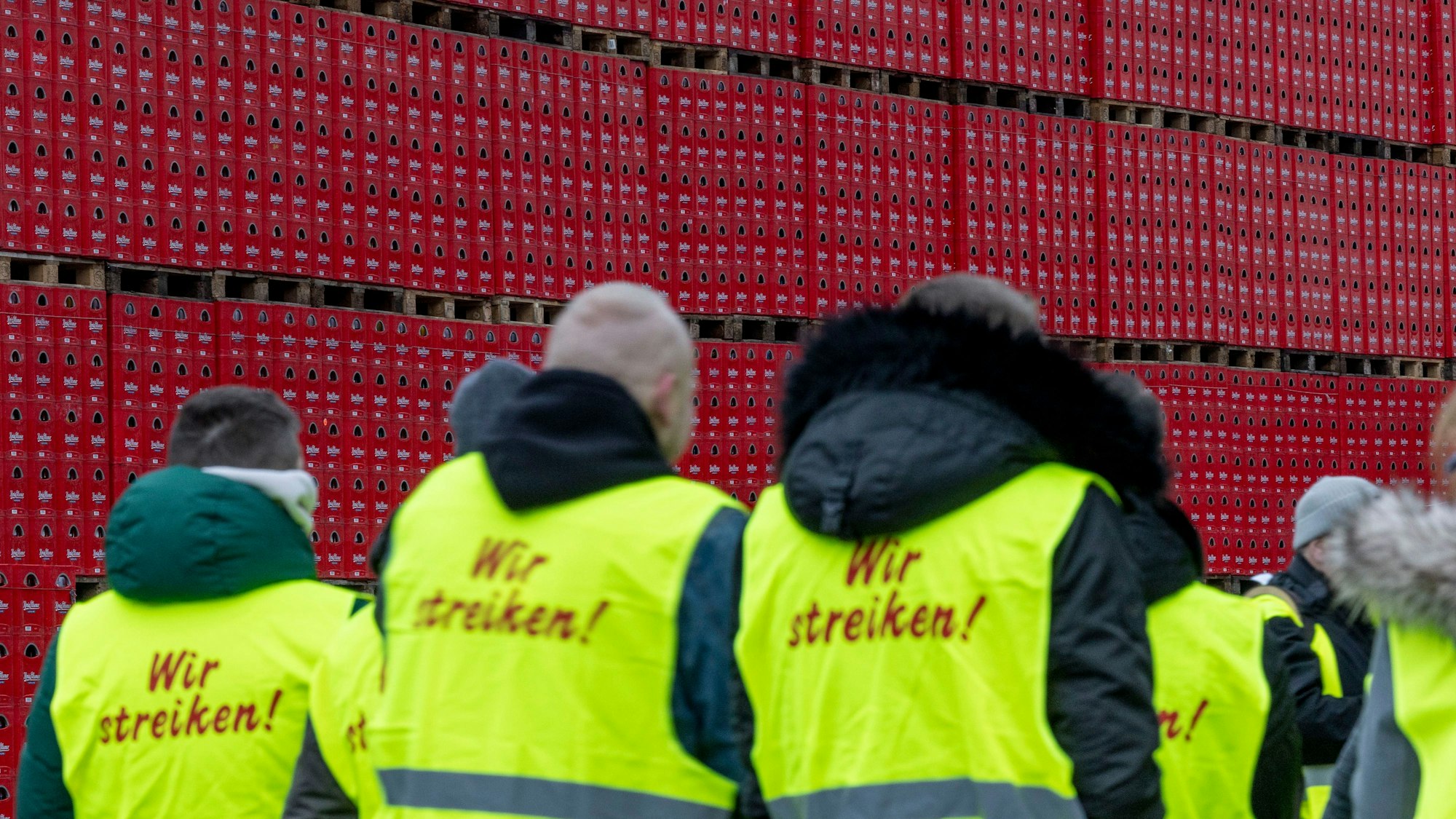 Mitarbeiter der König-Pilsener-Brauerei in Duisburg stehen in Warnwesten auf dem Betriebsgelände, im Hintergrund Bierkästen.