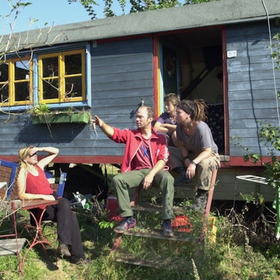Bewohner des Kasseler Bauwagenplatzes sitzen vor einem Wagen in der Sonne.