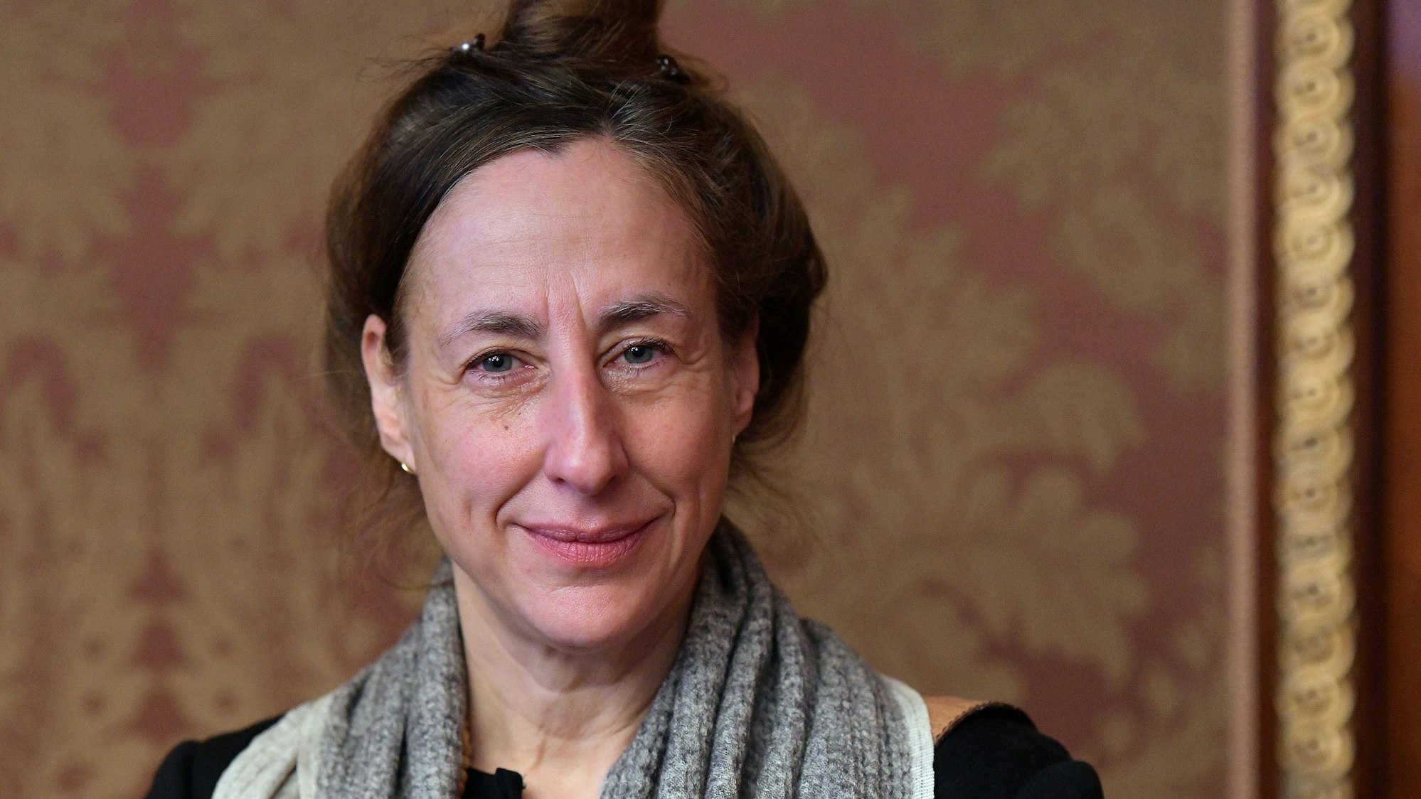 Judith Hermann steht vor einer Tapete mit rot-goldenen Ornamenten.