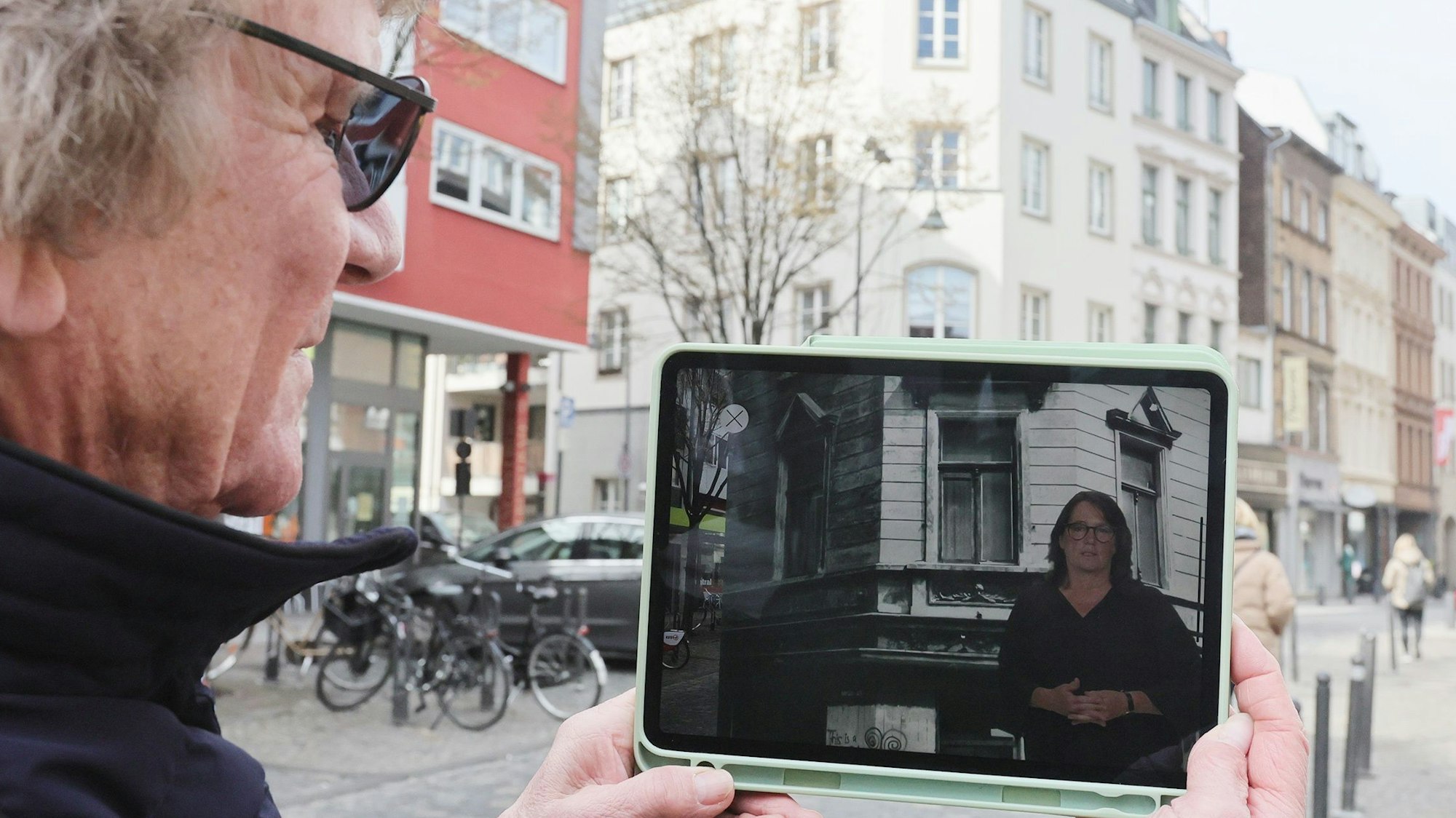 Bömmel Lückerath steht mit einem Tablet auf dem Severinskirchplatz.