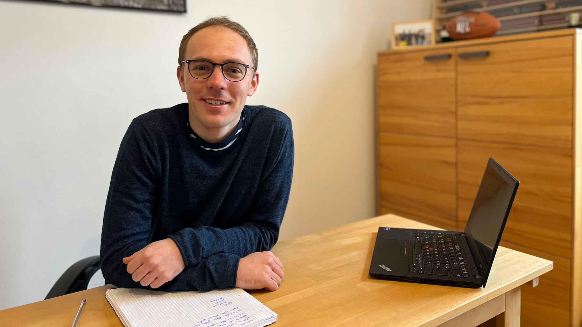 Tobias Ostlender sitzt an seinem Pult, vor ihm ein beschriebener Block, neben ihm ein geöffneter Laptop.