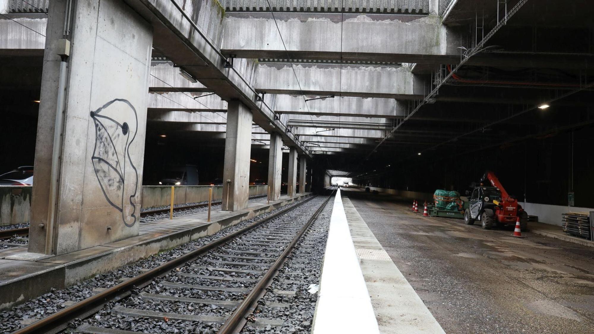 Ein Tunnel, in dem Schienen und eine Straße verlaufen. Am rechten Rand stehen Baufahrzeuge.