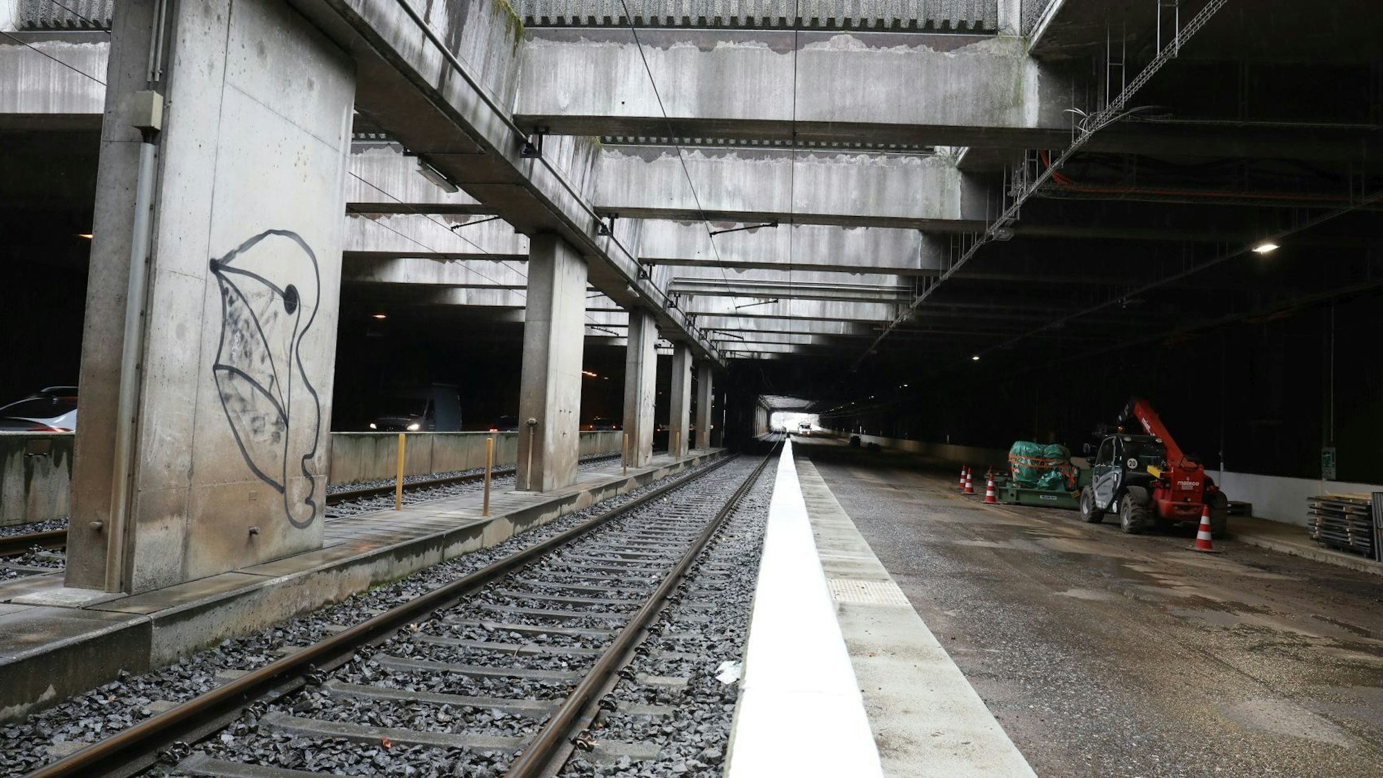 Ein Tunnel, in dem Schienen und eine Straße verlaufen. Am rechten Rand stehen Baufahrzeuge.