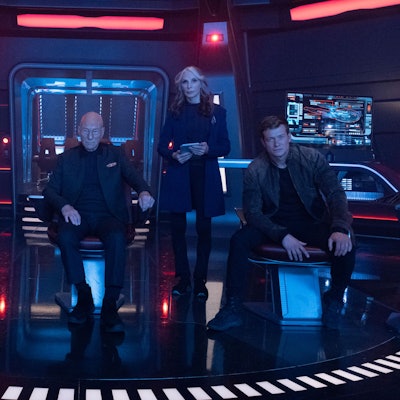 Joanthan Frakes, Patrick Stewart und Gates McFadden sind auf der Brücke eines Raumschiffes.