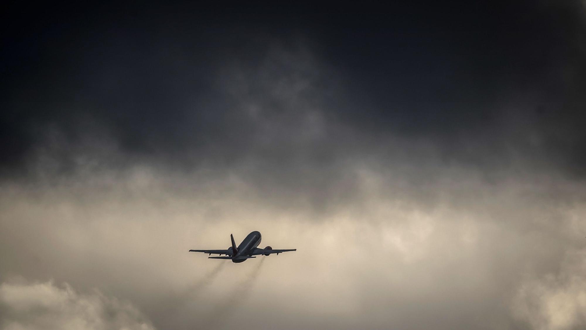 Ein Flugzeug fliegt nach dem Start auf eine dunkle Wolkenfront zu. (Symbolbild)