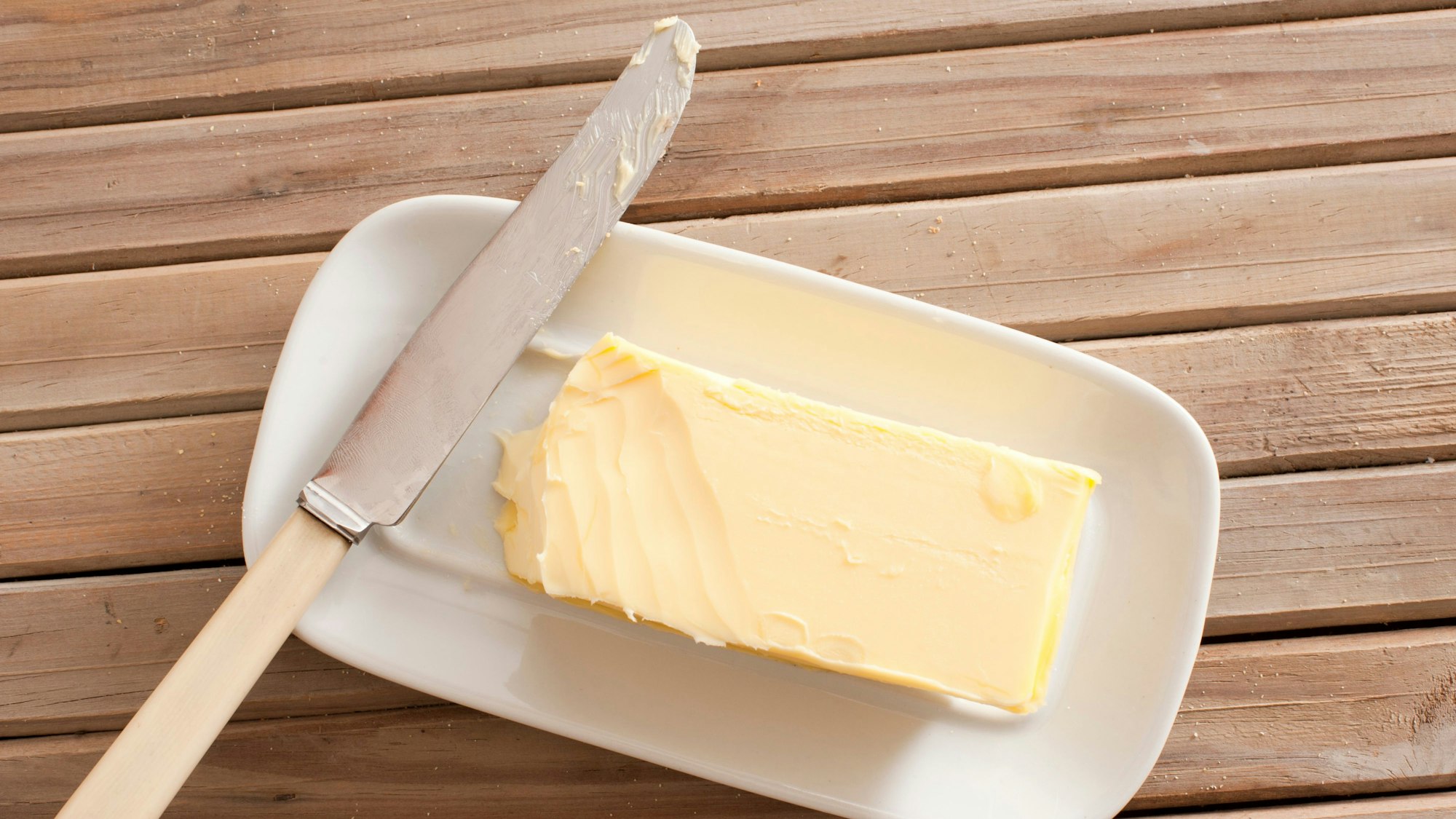 Ein Stück Butter und ein Messer liegen auf einem Teller.