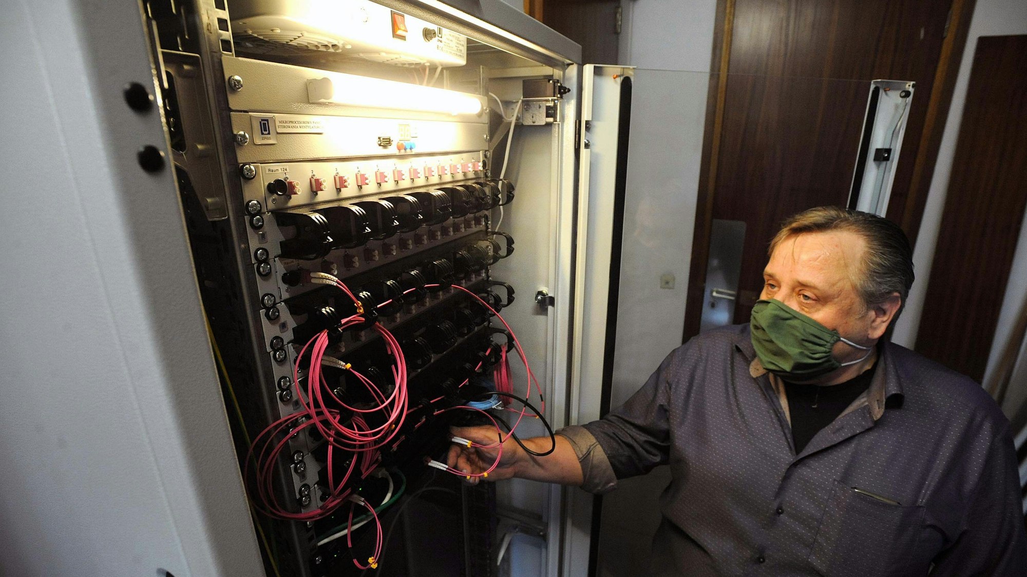 Jörg Brauckhoff steht mit Maske an der geöffneten Türe des Schaltschranks im Serverraum