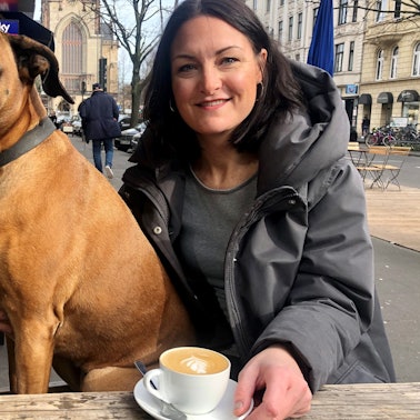 Junge Frau mit Boxer an einem Cafe draußen.