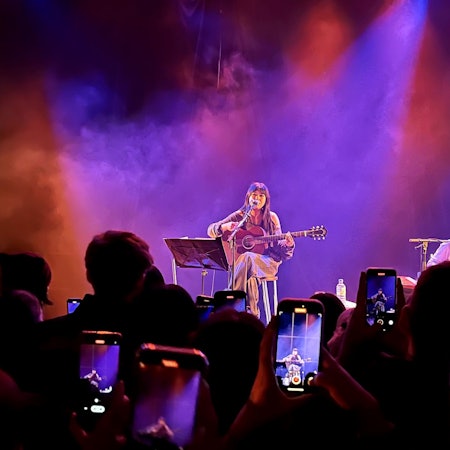 Die englische Sängerin Beabadoobee sitzt am 17. März 2023 mit einer Gitarre auf einem Barstuhl auf der Bühne des Kölner Bürgerhaus Stollwercks. Ihre Fans filmen sie mit ihren Handys ab.
