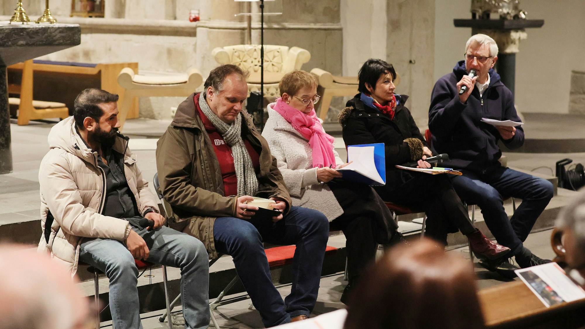 Fünf Menschen sitzen vor einem Altar auf Stühlen.