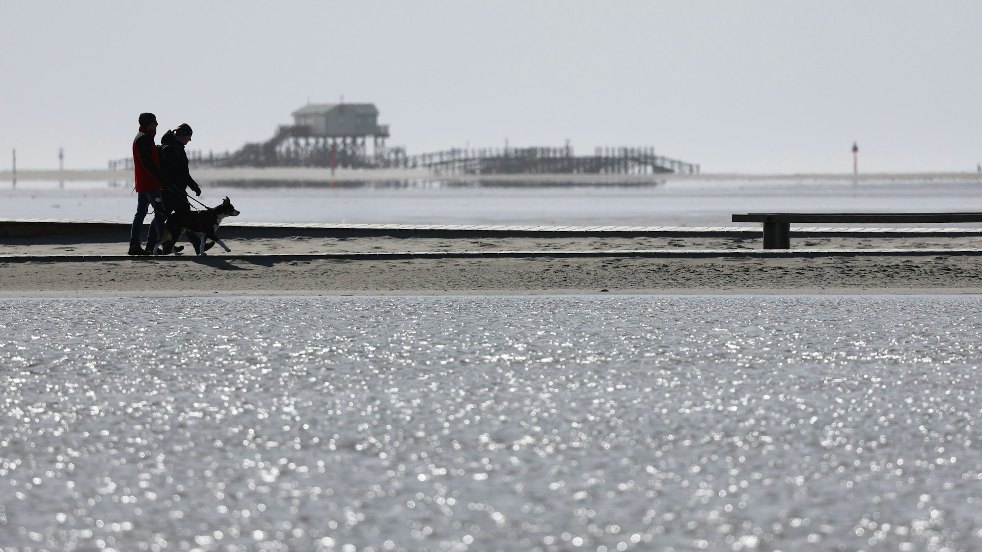 Menschen sind bei Sonnenschein und kühlem Wind am Nordseestrand unterwegs.