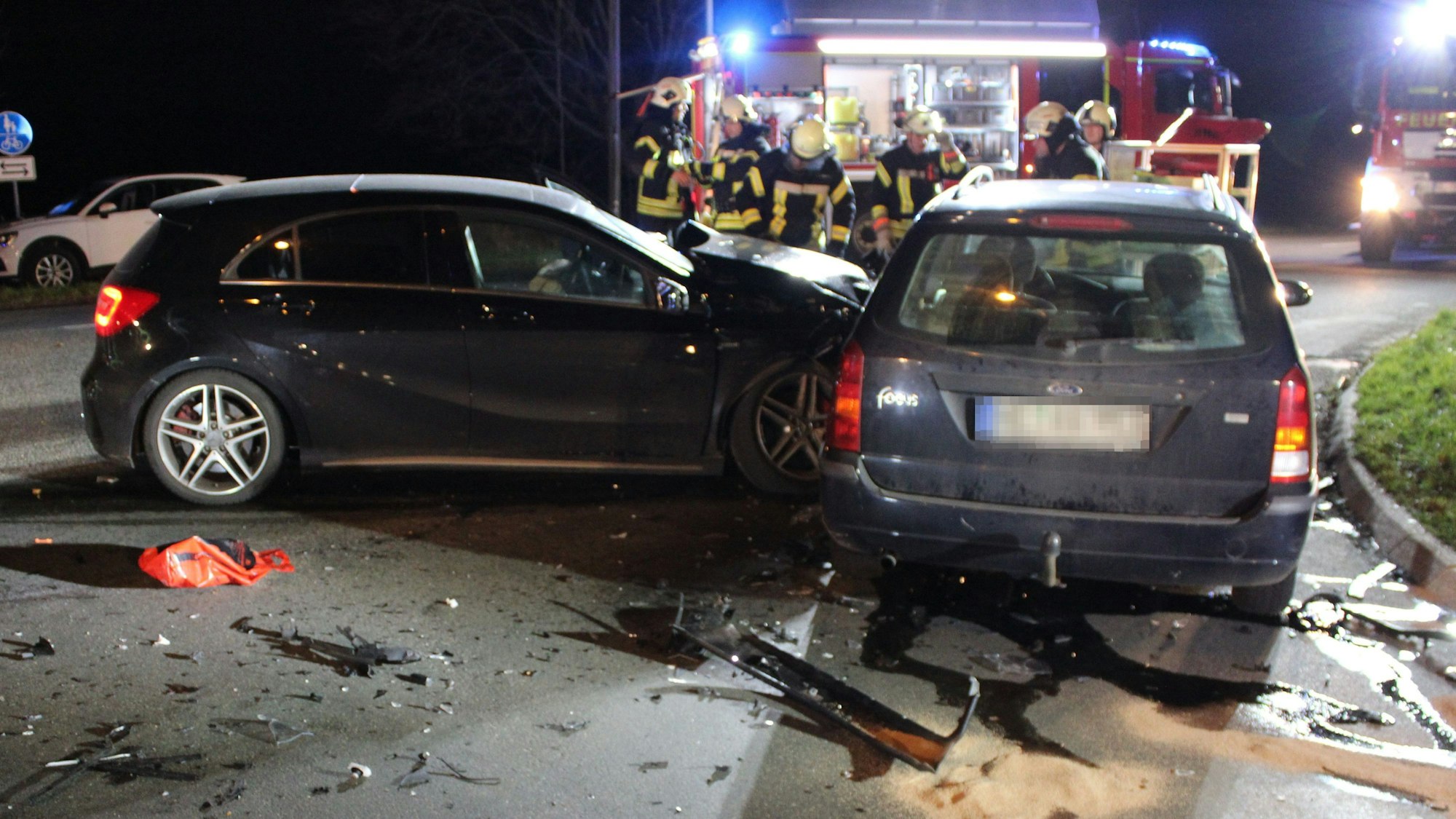 Die kollidierten Wagen auf der dunklen Straße, dahinter stehen Feuerwehrautos.