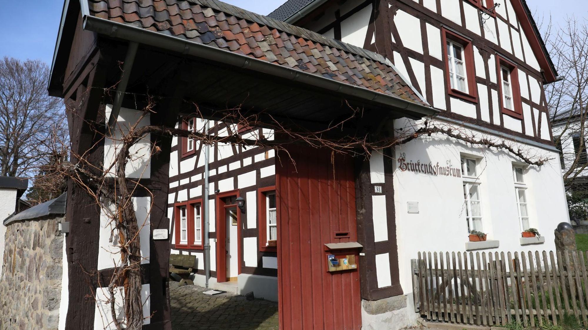 Über dem offenen Portal, das zu einem kleinen Hof führt, ranken Weinreben. Das Fachwerkhaus hat rote Fenstereinfassungen.