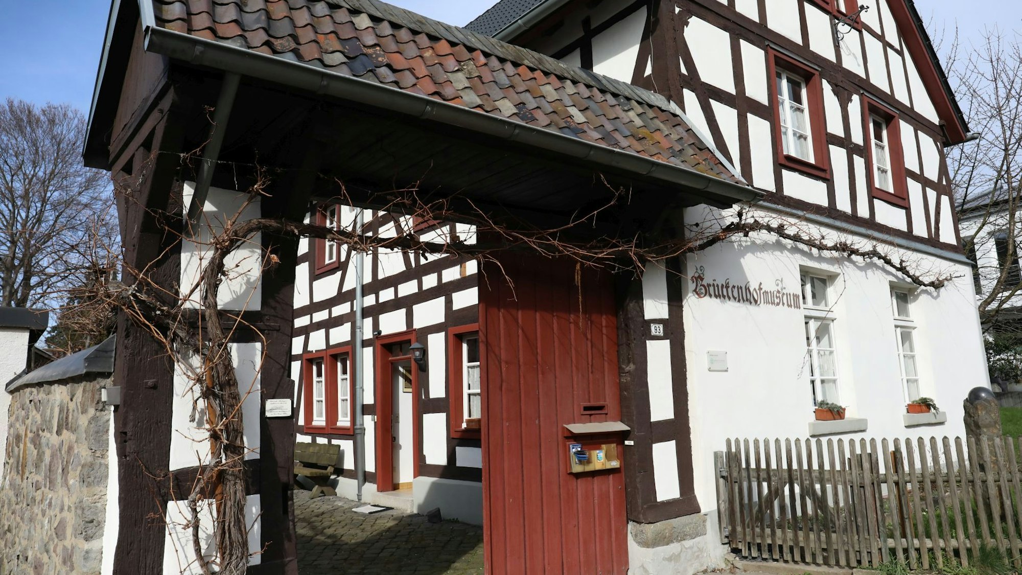 Über dem offenen Portal, das zu einem kleinen Hof führt, ranken Weinreben. Das Fachwerkhaus hat rote Fenstereinfassungen.