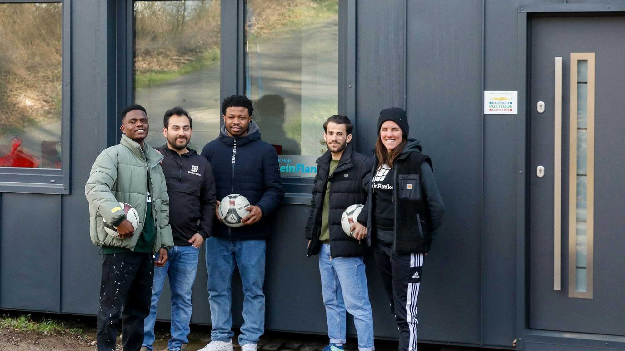 Judith Solf und Mahmoud Alkhallawi (2. von links) mit Justice, Ebuka und Road vor dem anthrazit-farbenen Hope Hub-Container am Sportgelände des ESV Köln.