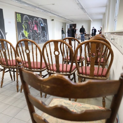 Im Vordergrund stehen in der ehemaligen Fabrikhalle braune Stühle, links an der Wand lehnen großformatige Streetart-Kunstwerke.