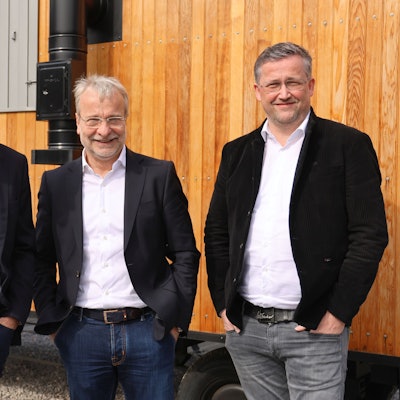 Gruppenfoto mit drei Herren vor einem Bauwagen.