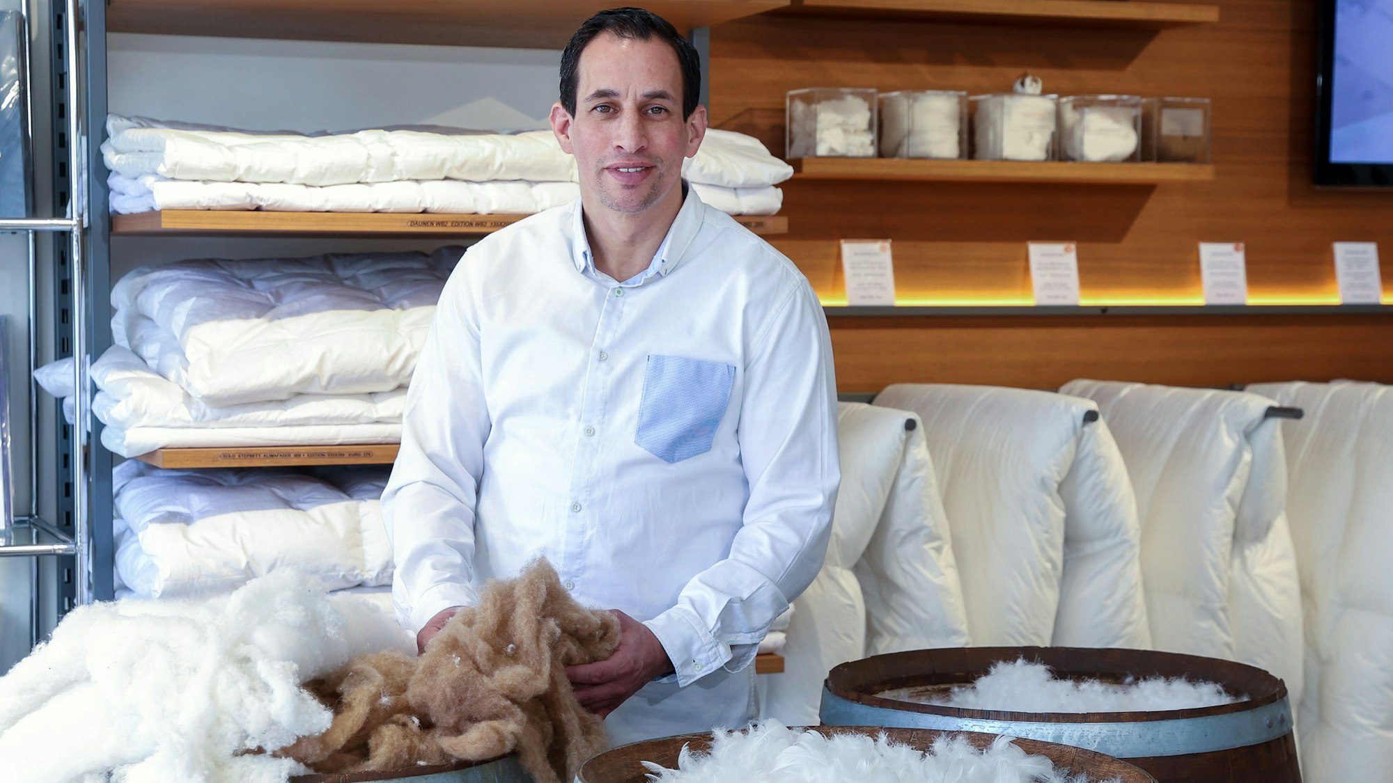 Inhaber Michael Gouram mit Fässern voller Daunen, im Hintergrund Daunendecken.