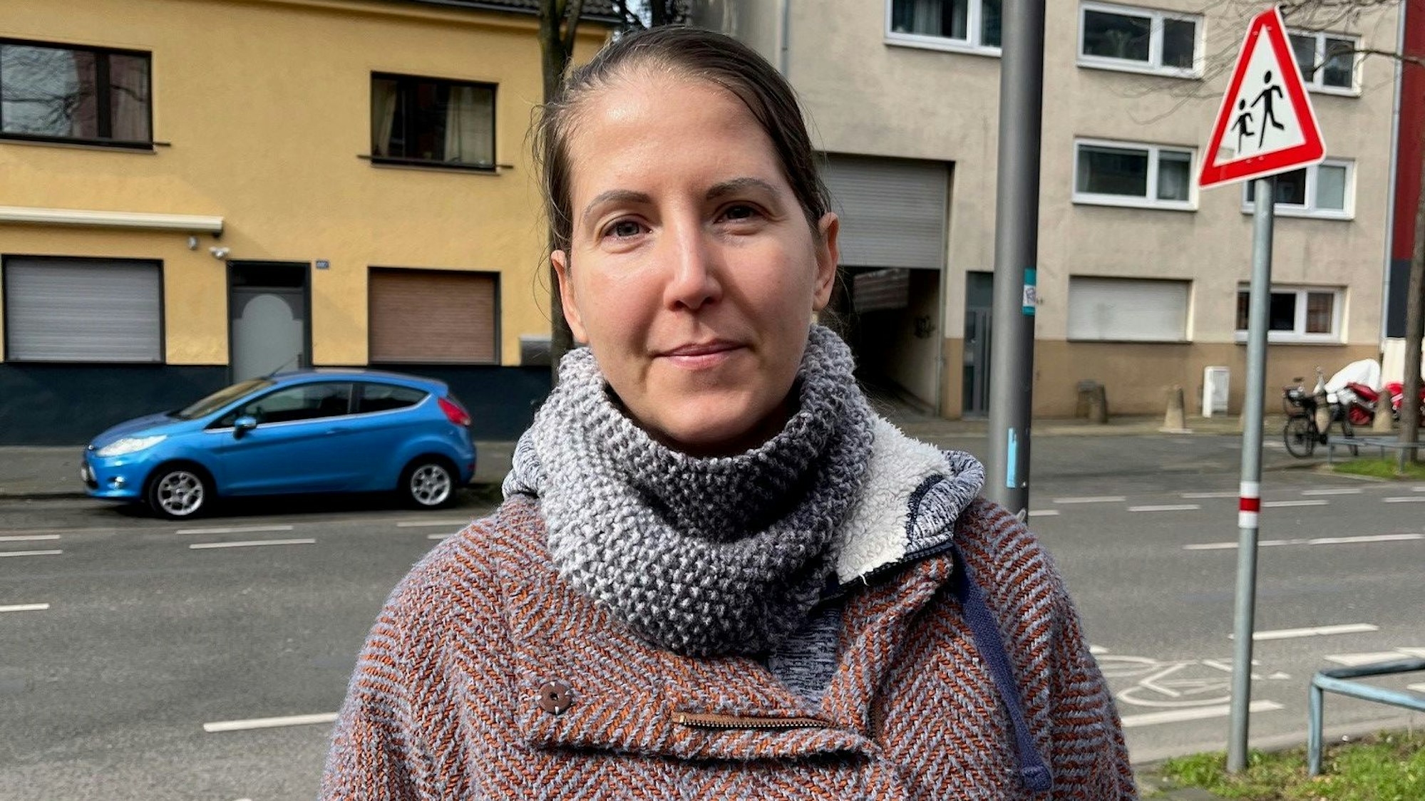 Agnes guckt in die Kamera. Sie steht an der Neusser Straße und trägt einen rotbraunen Mantel.