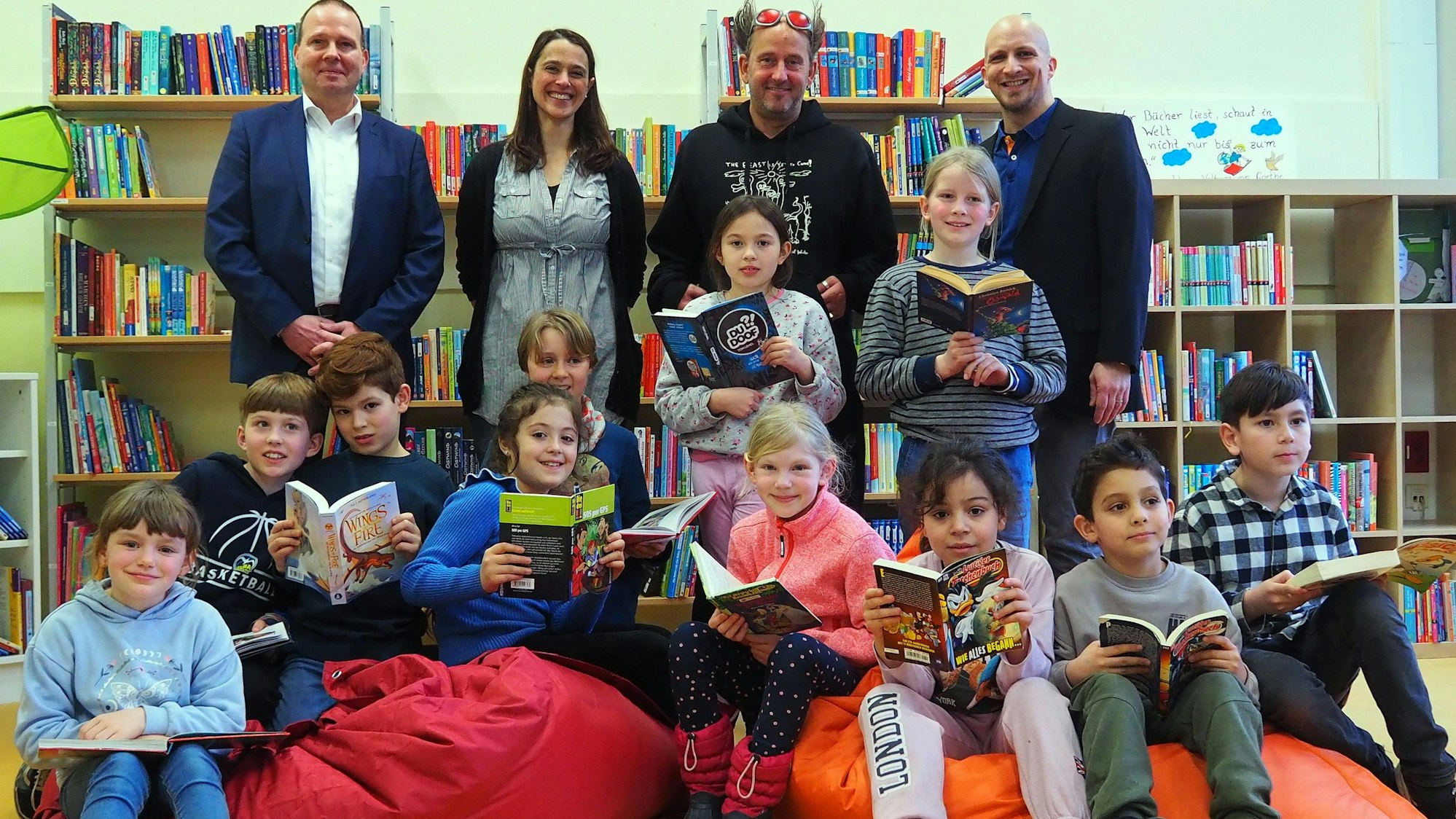 Kinder sitzen mit Büchern in der Hand auf bunten Sitzsäcken, dahinter stehen Lehrerinnen und Lehrer und Kika-Moderator Tom Lehel.