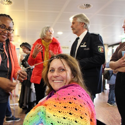 Epiphana Uwimana dreht einer in Regenbogenfarben gekleideten Besucherin bunte Fäden in die Haarsträhnen.
