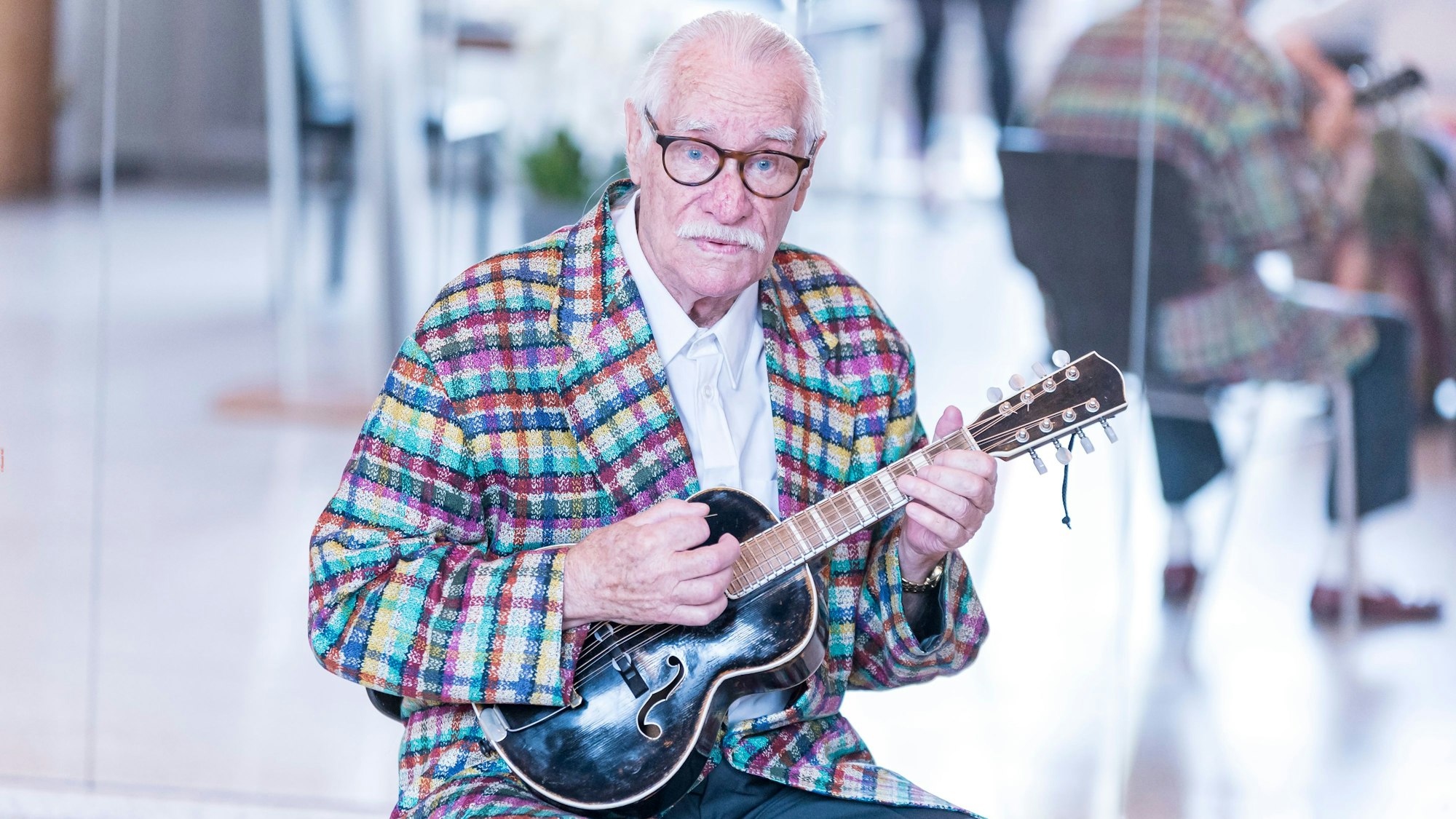 Hans Süper sitzt mit einer kleinen Gitarre im Muschelsaal des Historischen Rathauses zu Köln.
