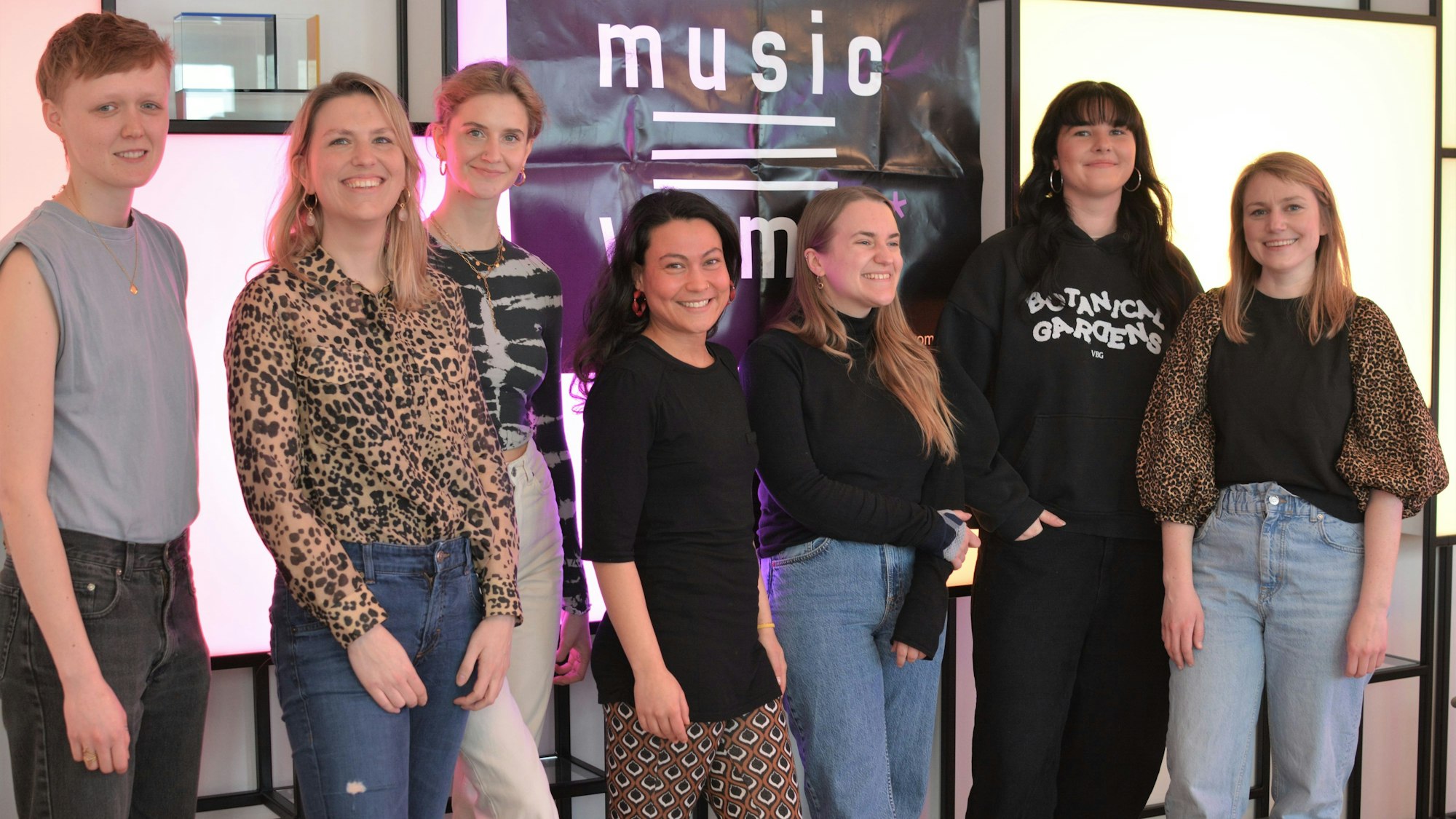 Sieben Frauen stehen beieinander und lachen in die Kamera.