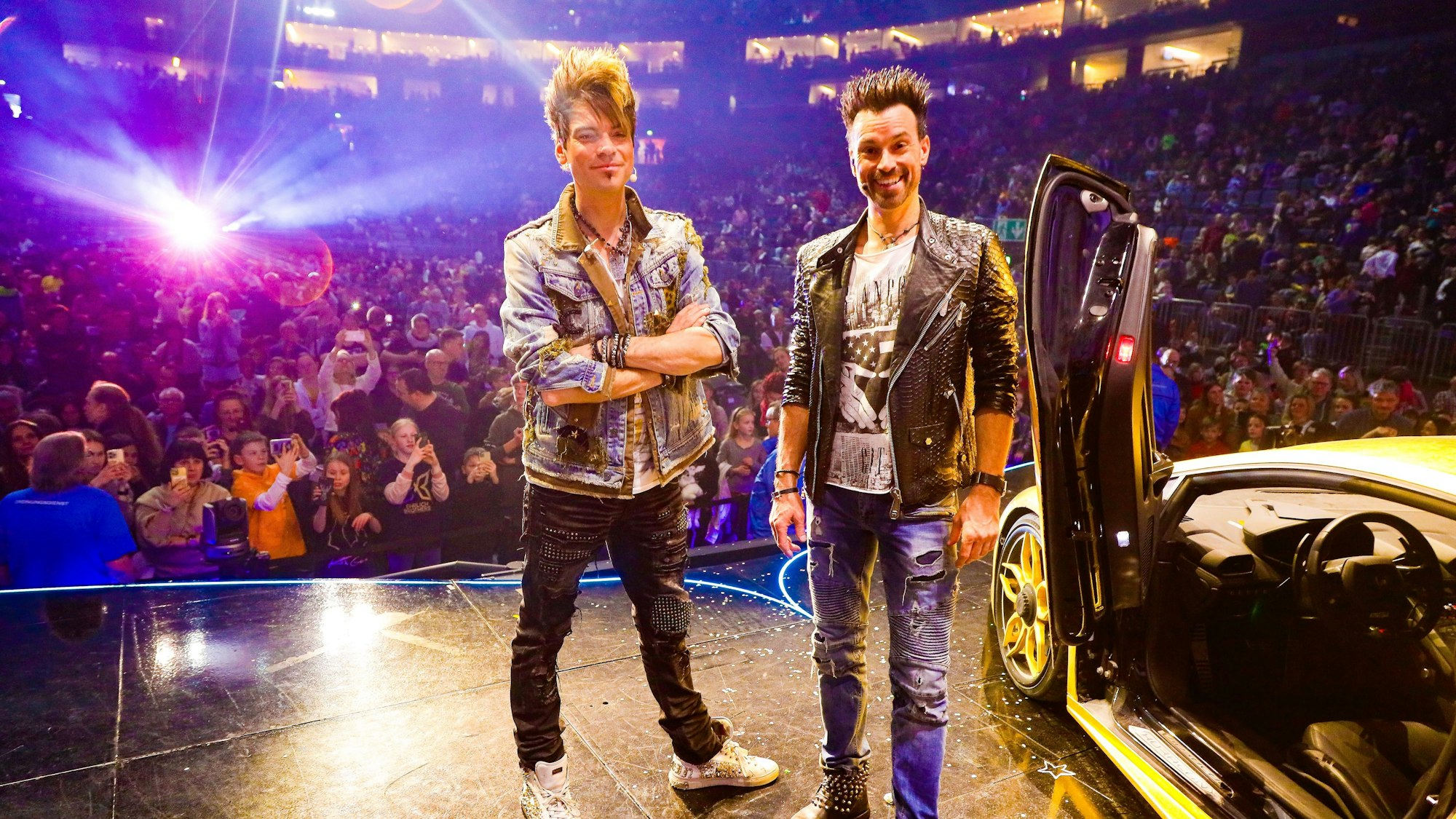 Die Ehrlich Brothers posieren in der Kölner Lanxess-Arena vor einem goldenen Lamborghini.